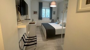 Een hotelkamer met een bed, nachtkastje, stoel, televisie, raam en gordijnen.