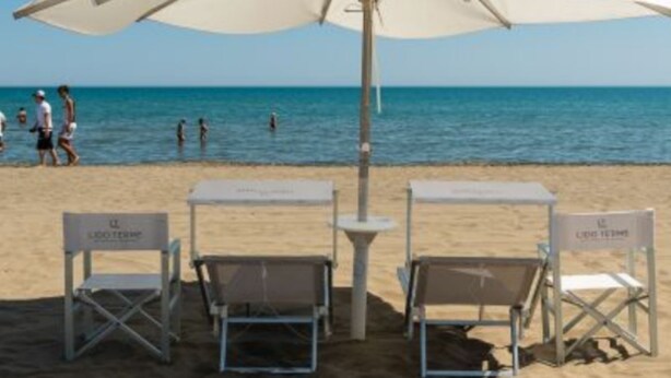 Een strand met witte parasols en stoelen, een heldere blauwe lucht en de oceaan op de achtergrond.