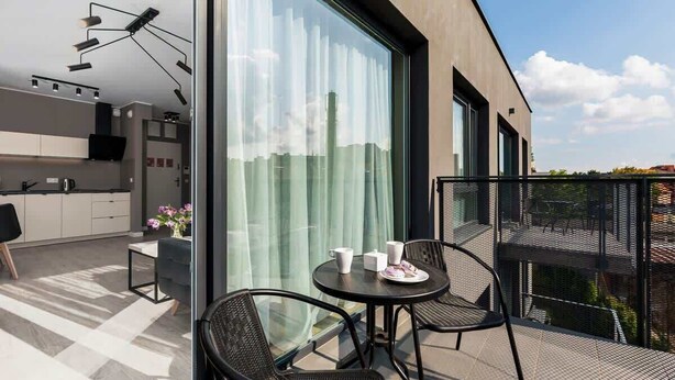 Ein moderner Balkon mit Esstisch und Stühlen, eine Küchenzeile mit Fernseher und große Fenster mit Blick auf die Stadt.