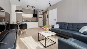 Ein modernes Wohnzimmer mit einem grauen Sofa, einem Couchtisch mit Blumenvase und einem Essbereich mit schwarzem Tisch und Stühlen.
