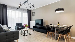 Ein modernes Wohnzimmer mit einer Couch, einem Couchtisch, einem Esstisch mit Stühlen, einem Fernseher und einer Pendelleuchte.