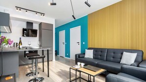 Una sala de estar moderna con un sofá de cuero negro, una mesa de centro de madera y una zona de cocina con un taburete de bar.