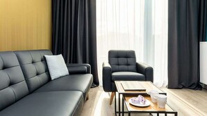Una sala de estar moderna con un sofá negro, un sillón negro y una mesa de centro de madera con un plato y tazas.