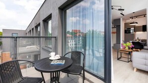 Un appartement moderne doté d’un balcon avec une table ronde et deux chaises, une grande porte-fenêtre coulissante et une vue sur le paysage urbain.