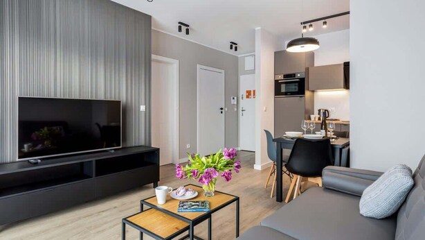 Un salon moderne avec un téléviseur à écran plat, une table basse et un canapé. Il y a également un coin repas avec une table et des chaises.