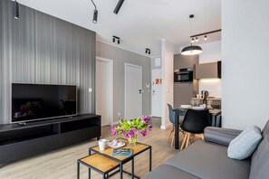 Una sala de estar moderna con una televisión de pantalla plana, una mesa de centro y un sofá. Hay un comedor con una mesa y sillas.