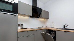 Une cuisine moderne avec des meubles de couleur grise, un four encastré, une hotte noire, un plan de travail en bois et un lave-vaisselle.