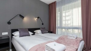 Habitación de hotel con cama doble, mesita de noche, lámpara y ventana con cortinas.