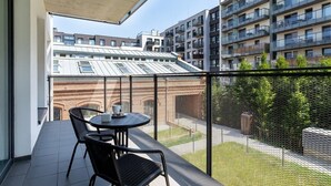 A balcony with a table and chairs, overlooking a courtyard with buildings in the background.