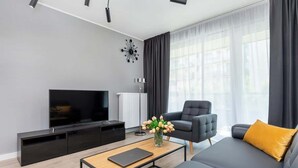 A modern living room with a flat-screen TV, a sofa, a coffee table, and a chair.