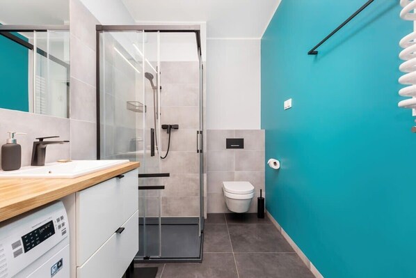 Un baño moderno con cabina de ducha de vidrio, inodoro y lavamanos con encimera de madera.