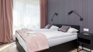 A modern bedroom with a large bed, two bedside lamps, a nightstand, and a window with curtains.