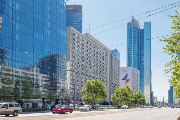 A modern urban street with high-rise buildings, including a hotel with a visible logo and a large glass facade.
