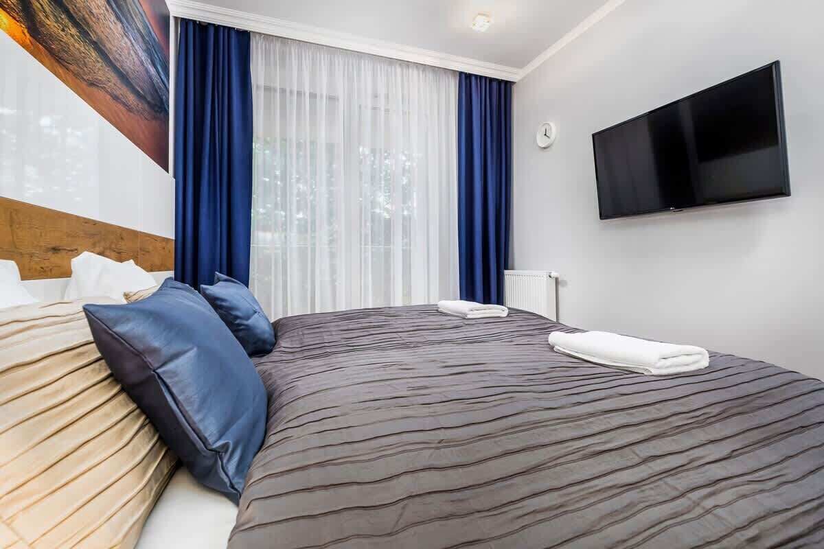 Ein Hotelzimmer mit einem großen Bett, einem Flachbildfernseher und einem Fenster mit durchsichtigen Vorhängen.