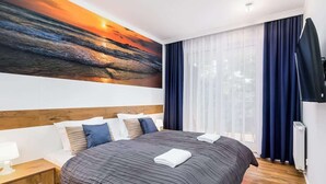 Una camera d'albergo con un letto grande, un comodino, un quadro raffigurante un tramonto e vista sull'esterno attraverso una finestra con tende.