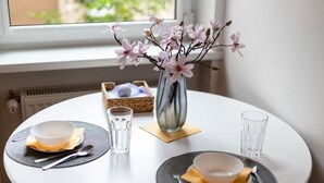 A round dining table with two plates, each with a bowl and cutlery, and a vase with pink flowers. - Stylish Studio | Next to Wilson Park and MTP Fair. (Poznan)