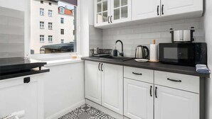A compact kitchen with white cabinets, a black countertop, and a window with a view of a building. - Stylish Studio | Next to Wilson Park and MTP Fair. (Poznan)