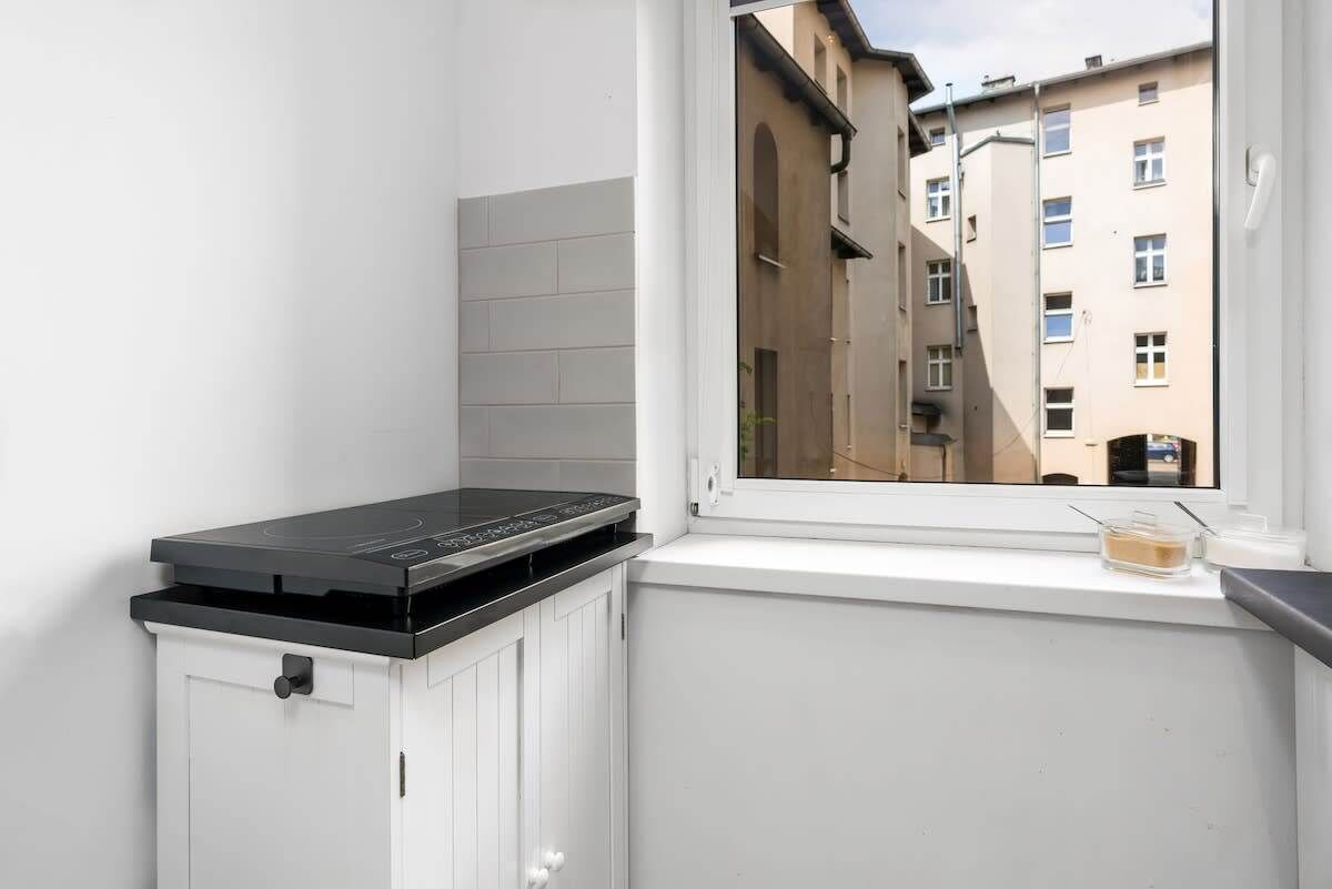 A kitchen with a built-in stove, white cabinets, and a window overlooking a narrow street with buildings.