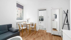 A modern living room with a grey sofa, a round wooden table with chairs, a large mirror, and a kitchenette in the background. - Stylish Studio | Next to Wilson Park and MTP Fair. (Poznan)