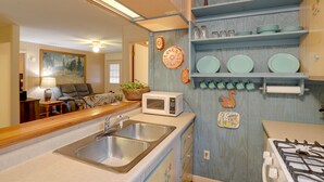 A kitchen with a sink, microwave, and stove. There are shelves with dishes and a painting on the wall. - Carolina Country Cabin! Hot Springs Getaway (Hot Springs)