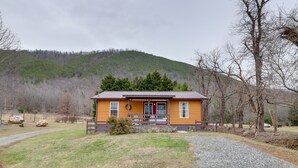 A wooden cabin with a red door, surrounded by a gravel driveway and a forested hill in the background. - Carolina Country Cabin! Hot Springs Getaway (Hot Springs)