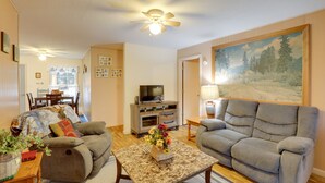 A living room with two sofas, a coffee table with a floral arrangement, a television on a wooden cabinet, and a painting on the wall. - Carolina Country Cabin! Hot Springs Getaway (Hot Springs)