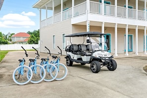 A building with a porch, a golf cart, and four bicycles parked in front.