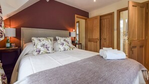 A neatly made bed with floral pillows, a bedside table with a bottle, and a wooden wardrobe in a hotel room.