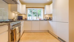 Una cocina moderna con armarios blancos, estufa, horno y ventana con vista a la vegetación.