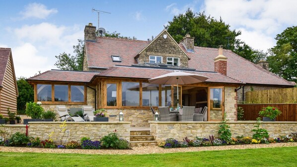 A two-story house with a stone facade, large windows, and a covered patio area with outdoor furniture.