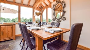 Un comedor con una mesa de madera dispuesta para cuatro personas, rodeada de sillas oscuras, bajo un techo de madera con vigas a la vista.