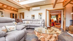 Un salón espacioso con un amplio sofá gris en forma de L, una mesa de centro de vidrio con base de madera natural y vistas a un comedor a través de un arco.