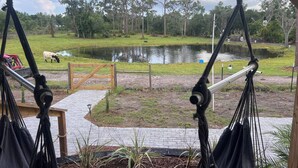A hammock chair overlooking a pond with a wooden gate and a grassy area with trees. - Lake Side Tiny home in Punta Gorda, Florida (Punta Gorda)