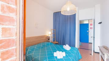 Ein Hotelzimmer mit einem Bett, einem blauen Vorhang, einem hölzernen Kopfteil, einem Nachttisch mit einer Lampe und einer Tür zu einem anderen Raum.