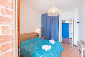 Ein Hotelzimmer mit einem Bett, einem blauen Vorhang, einem hölzernen Kopfteil, einem Nachttisch mit einer Lampe und einer Tür zu einem anderen Raum.