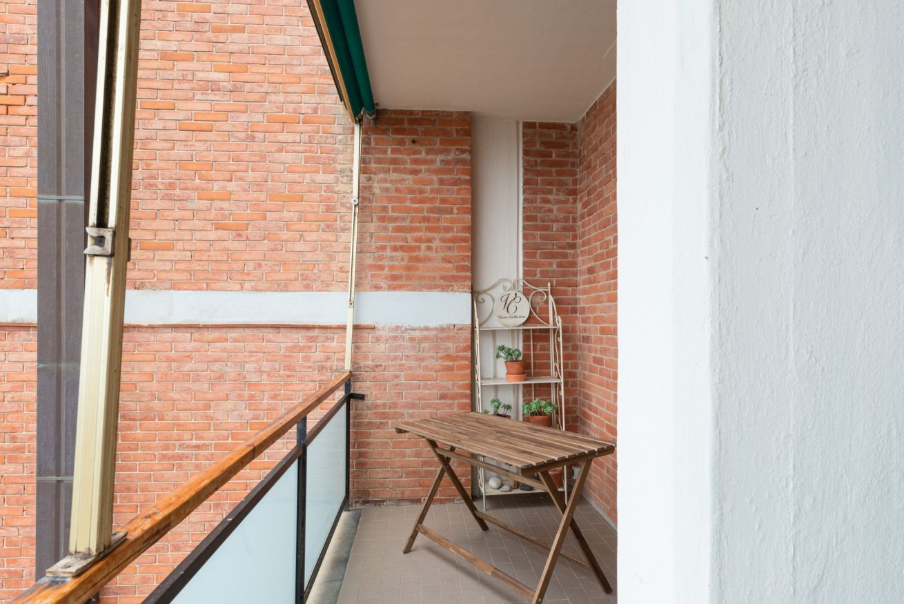 Un balcon avec une table en bois et une étagère en métal où sont disposées des plantes en pot.