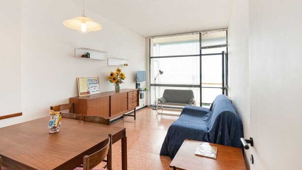 Ein Zimmer mit einem Holzesstisch, einer Couch, einem Schreibtisch und einem Fenster mit Jalousien.