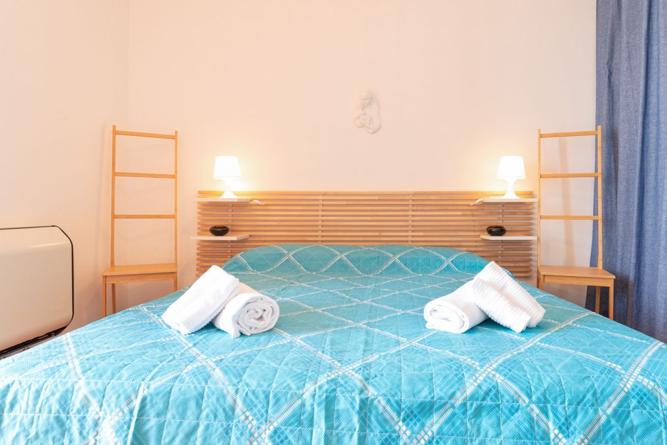 Un lit bien fait, recouvert d’une couette bleue, avec deux lampes de chevet et une tête de lit en bois.