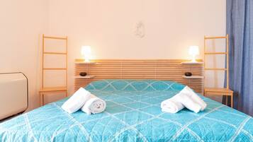 Un lit bien fait, recouvert d’une couette bleue, avec deux lampes de chevet et une tête de lit en bois.