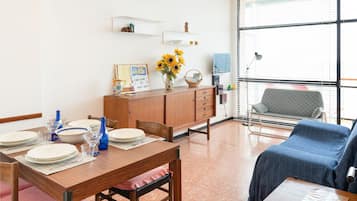 Ein Essbereich mit einem Holztisch, gedeckt für vier Personen, einer Couch und Blick ins Freie durch große Fenster.