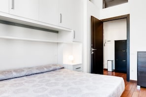 Une chambre à coucher comprenant un lit, une table de chevet, une armoire et une porte donnant sur une autre pièce.