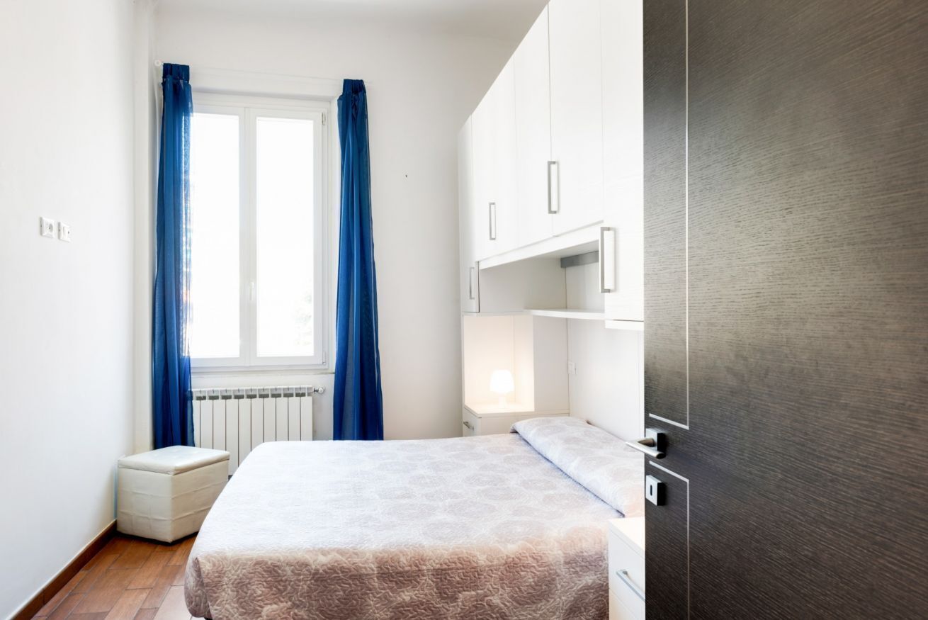 A bedroom with a bed, a nightstand, a dresser, and a window with curtains.