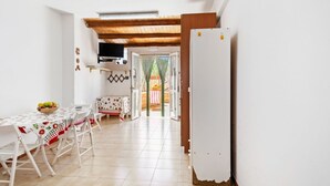 Uma cozinha com geladeira branca, mesa de jantar com cadeiras e uma TV fixada na parede.