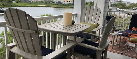 Een balkon met Adirondack-stoelen en een tafel, met uitzicht op een wateroppervlak en gebouwen.