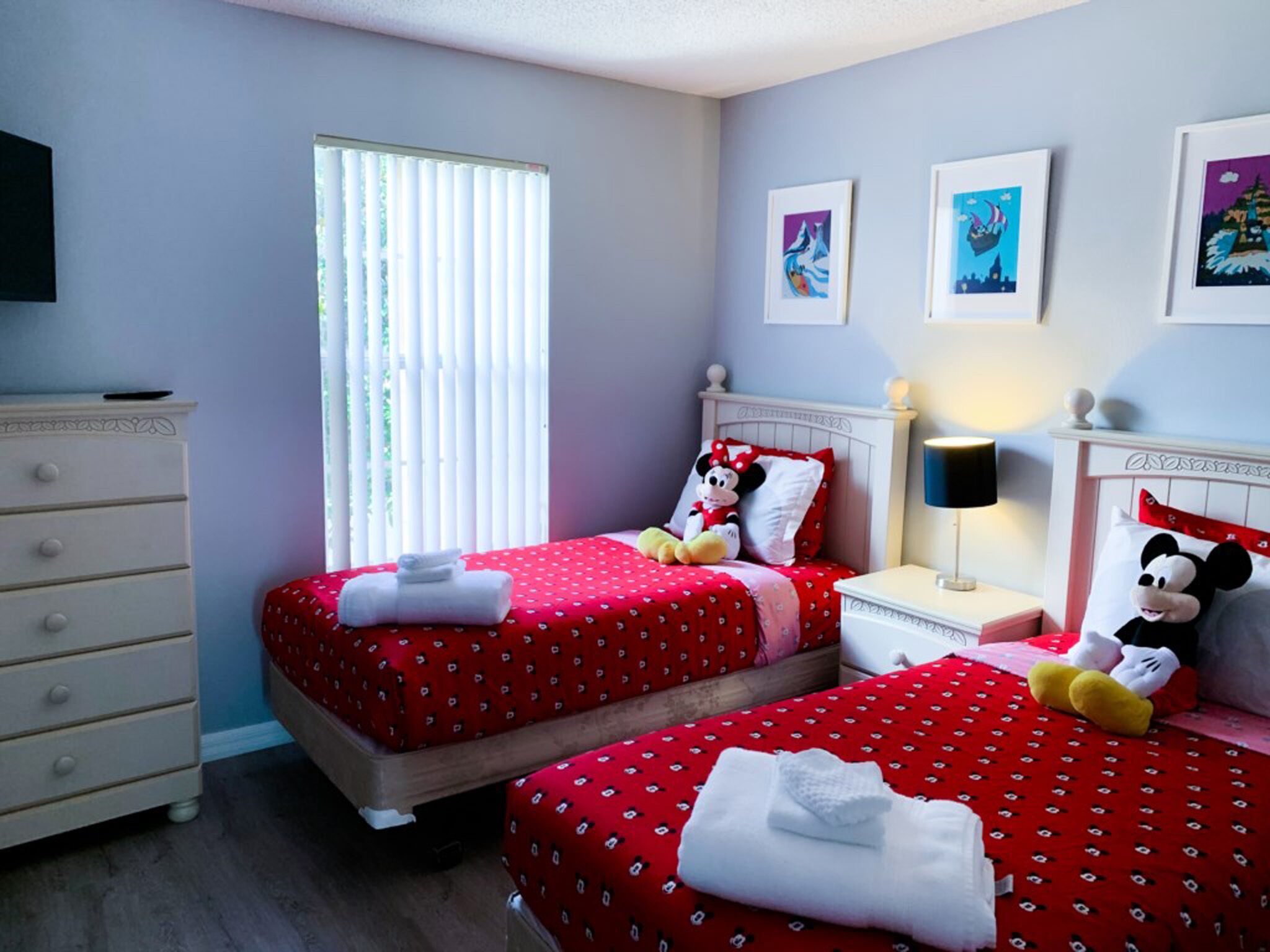 A hotel room with two beds, a dresser, a window with blinds, and wall art.