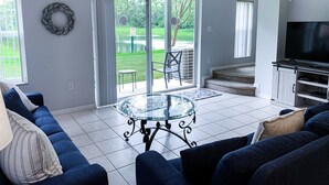A living room with a glass-top coffee table, a dark blue sofa, and a flat-screen TV. - Luxury Lake View 3 bedroom in resort community. Disney 3 miles (Kissimmee)