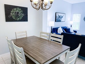A dining area with a wooden table and white chairs, a blue sofa, and a chandelier. - Luxury Lake View 3 bedroom in resort community. Disney 3 miles (Kissimmee)