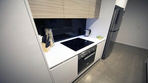 A modern kitchen with a black induction cooktop, a stainless steel refrigerator, and white cabinetry. - PENTHOUSE STYLE 4 BEDROOMS! (Bundall)