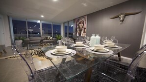 A modern dining area with a glass table set for six, surrounded by a city view. - PENTHOUSE STYLE 4 BEDROOMS! (Bundall)
