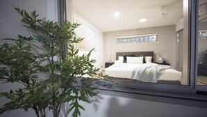 A modern hotel room with a large bed, a nightstand, a bedside table, and a window with a view of the room. - PENTHOUSE STYLE 4 BEDROOMS! (Bundall)